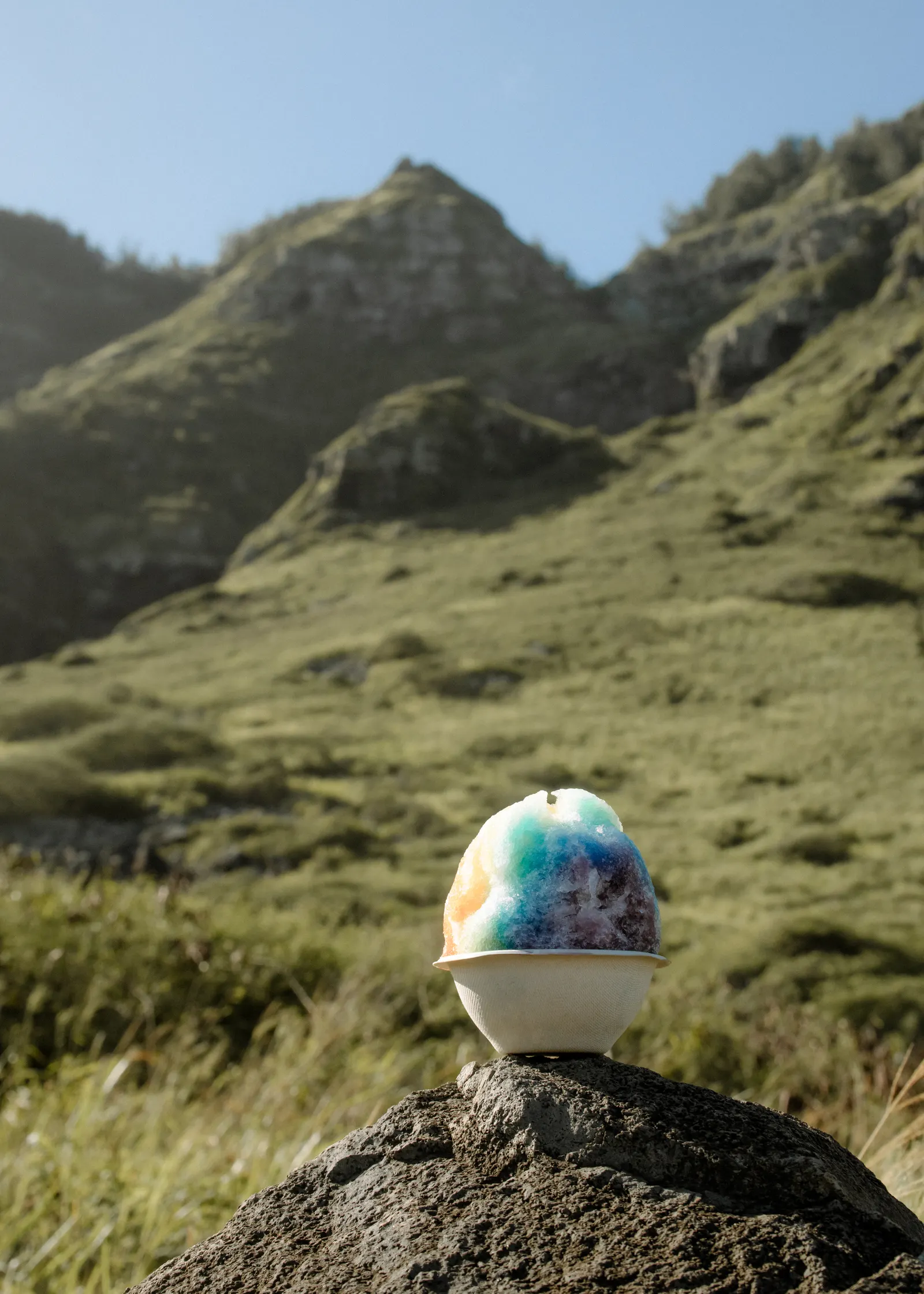 A rainbow shave ice resting on a rock in the mountains
