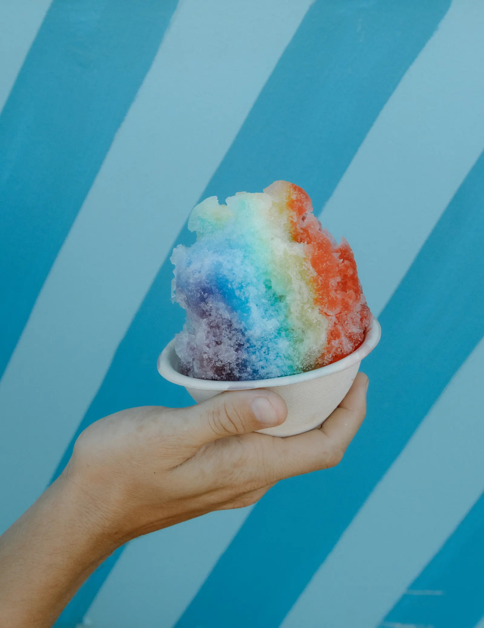 Rainbow shave ice held against the truck’s blue stripes
